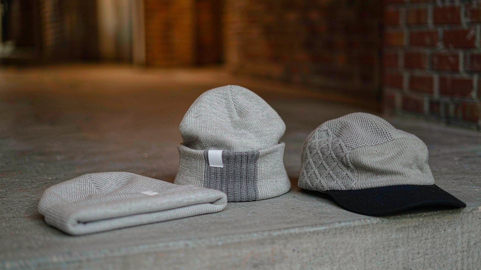 A ribbed beanie and a plain cap resting on a concrete ledge in soft hazy city light