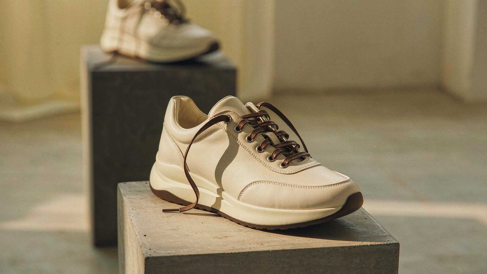 A single sneaker displayed on a concrete pedestal in a gallery-like space with dramatic side lighting