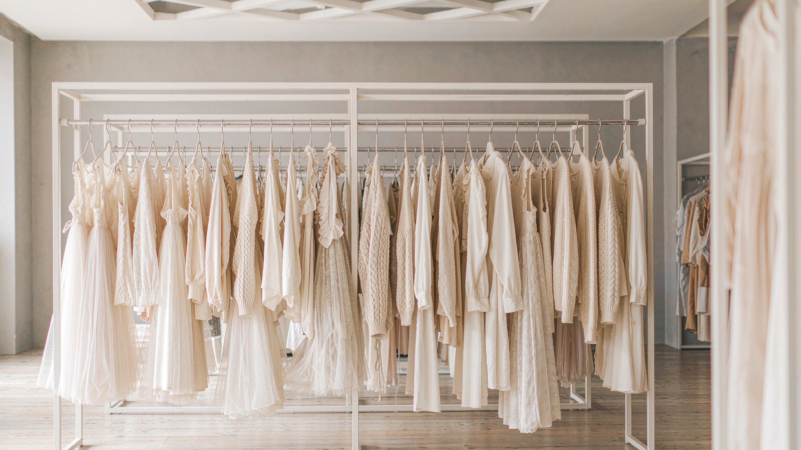 A clothing rail of neutral garments with small reduced-price tags in a bright minimal store with soft daylight