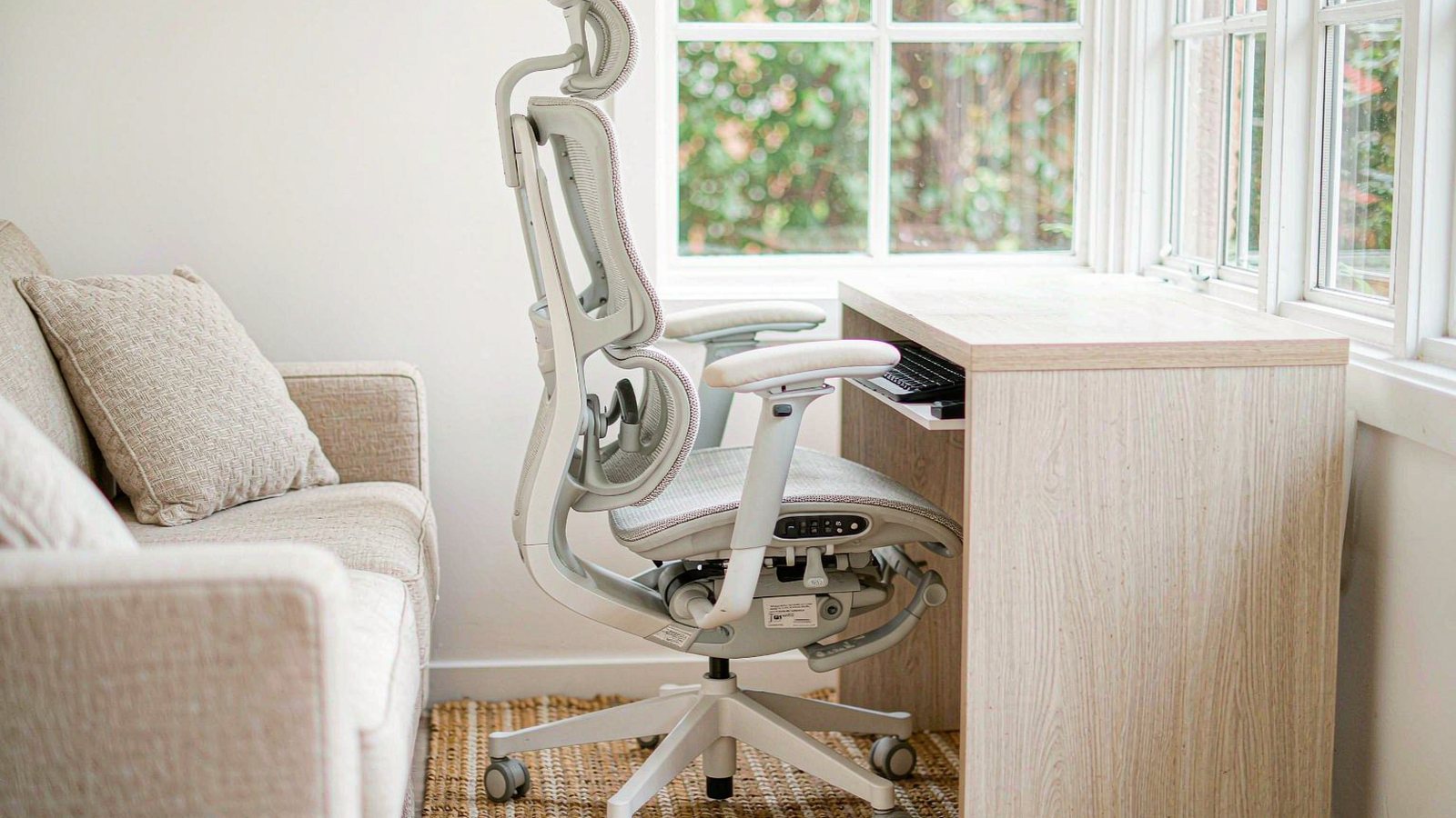 A mesh ergonomic office chair beside a wooden desk in a sunlit room with a woven rug on the floor