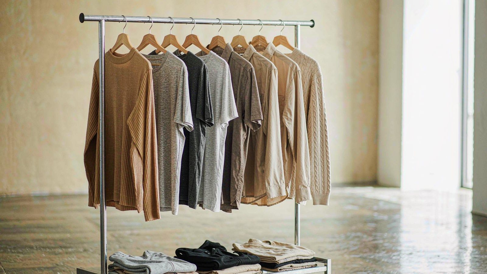 A rail of neutral streetwear pieces in a minimal showroom with a polished concrete floor and soft daylight