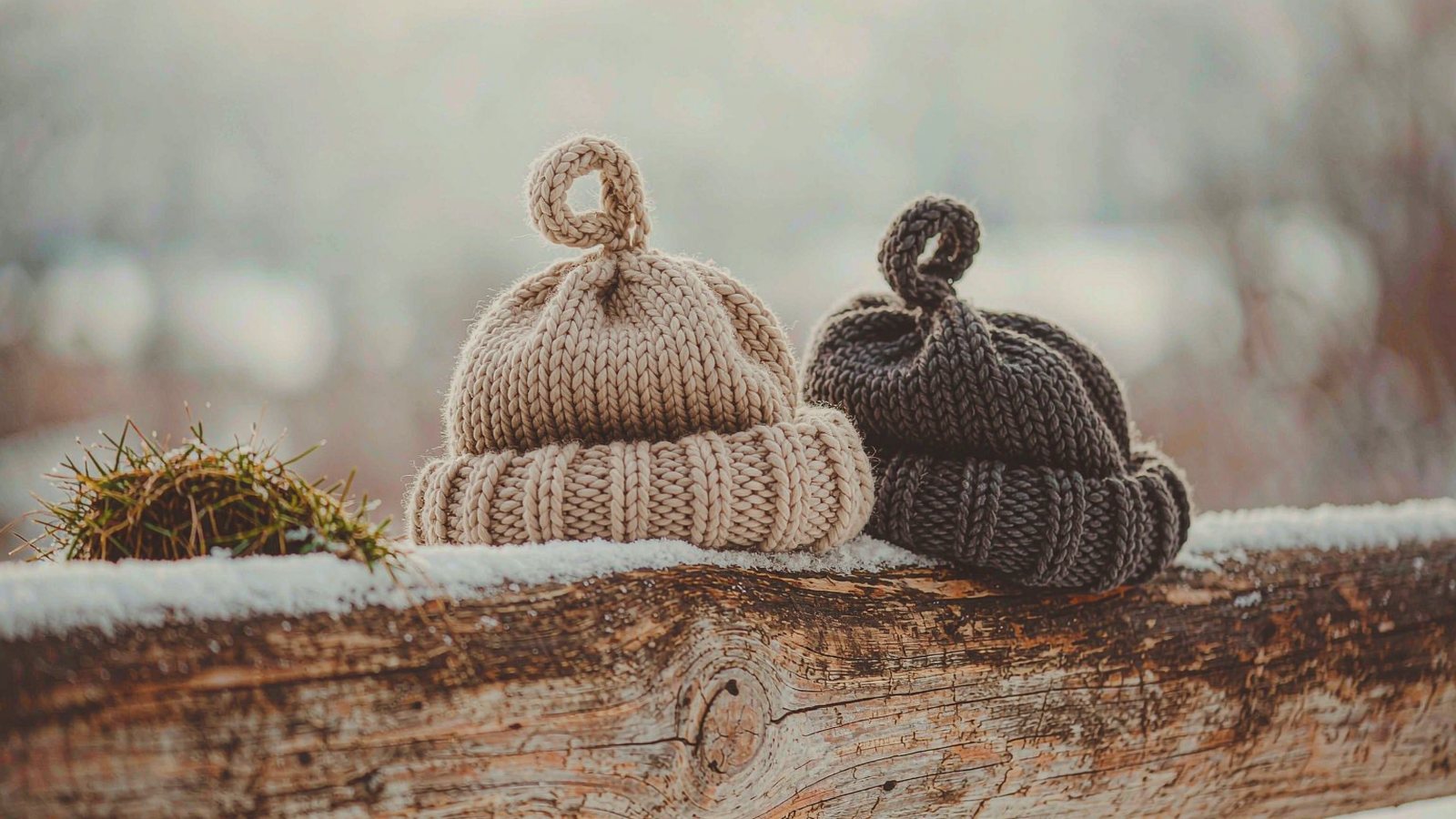 Chunky knit beanies resting on a snow-dusted wooden fence rail in soft winter light.
